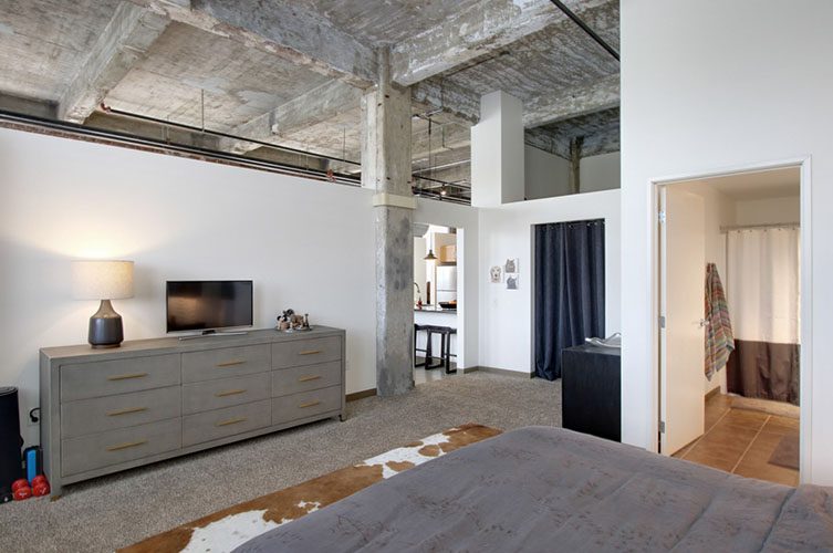 Interior of a luxury furnished loft at The Cork Factory in the Pittsburgh Strip District, featuring industrial concrete ceilings, modern furniture, and open-concept living.