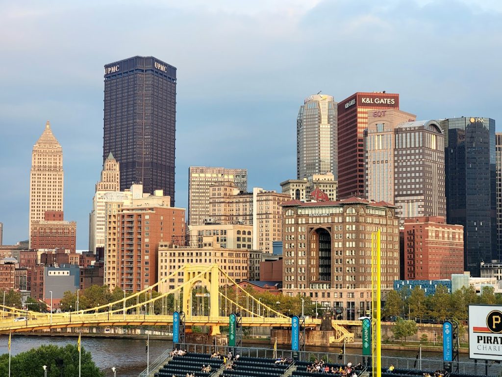 Panoramic view of downtown Pittsburgh skyline from the PNC Park, featuring the yellow Roberto Clemente Bridge and the UPMC building over the Allegheny River.