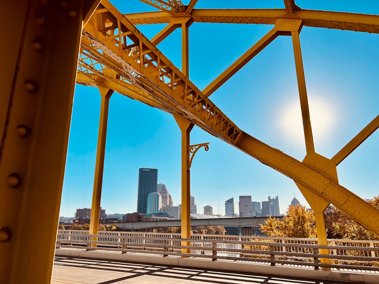 Close-up architectural view of a yellow sister bridge in Pittsburgh reflecting on the Allegheny River during a sunny afternoon.